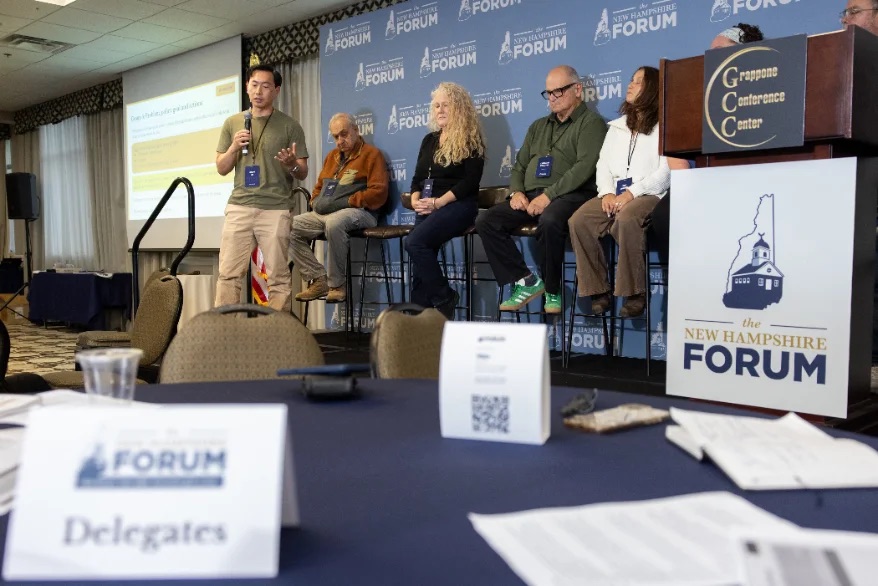 A delegate speaks during a plenary discussion as a panel looks on